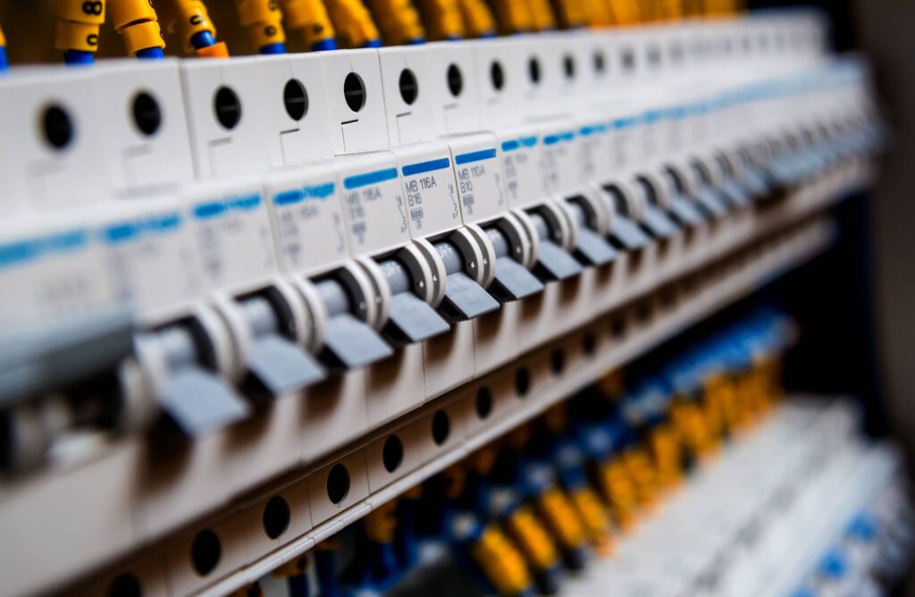 Close-up view of multiple circuit breakers arranged in a row inside an electrical panel, with yellow and blue labeled wires visible in the background.