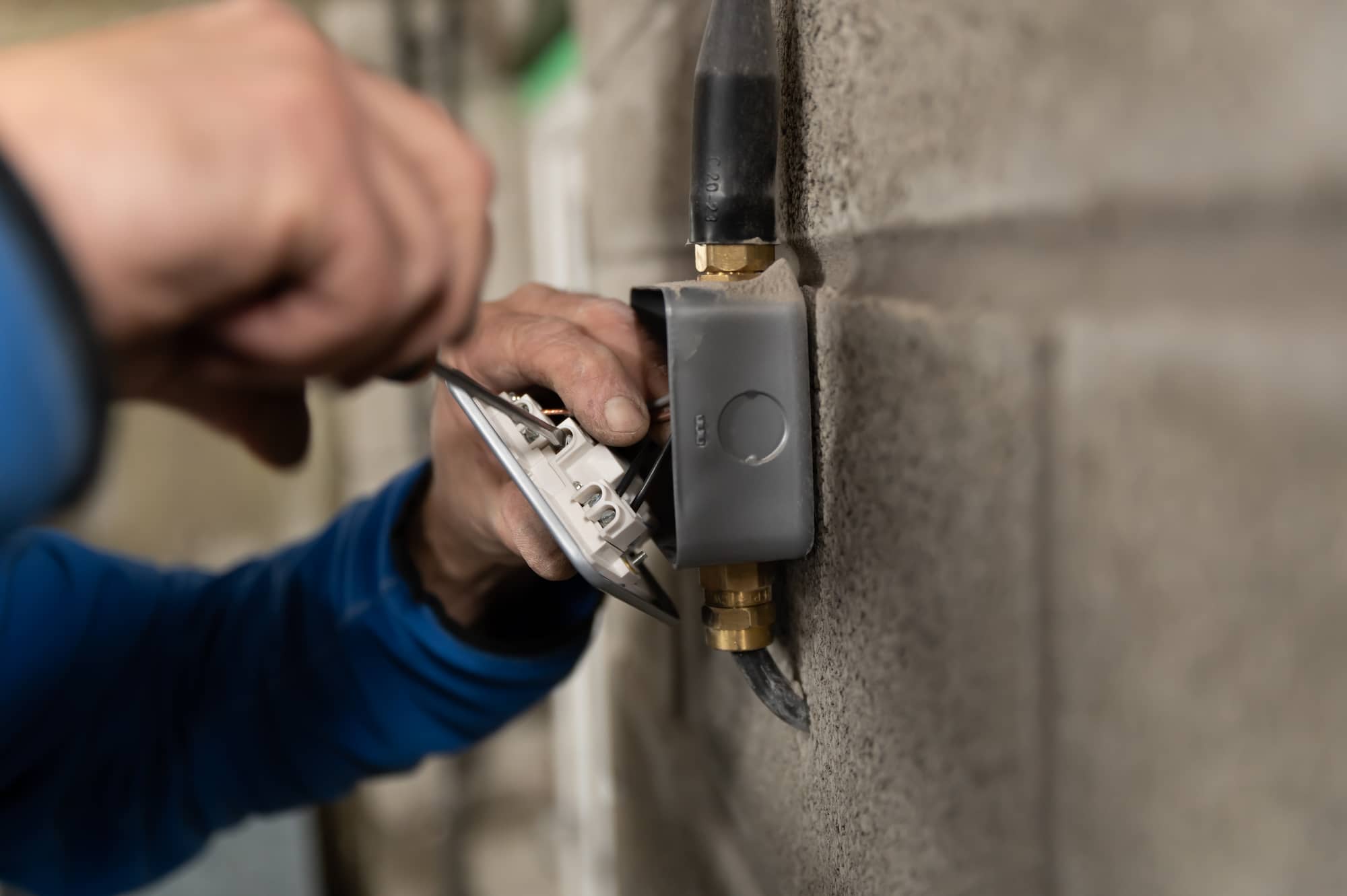 A person uses a screwdriver to install or repair an electrical outlet on a gray concrete wall.